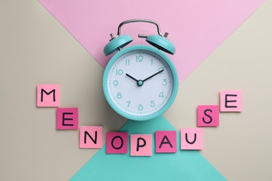 Photo of Pink paper notes with word Menopause and alarm clock on color background, flat lay