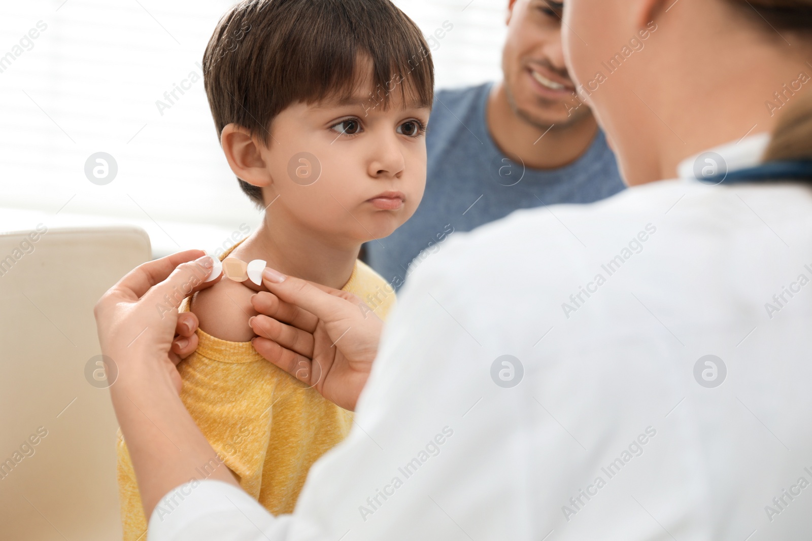 Photo of Doctor putting sticking plaster onto little boy's shoulder indoors