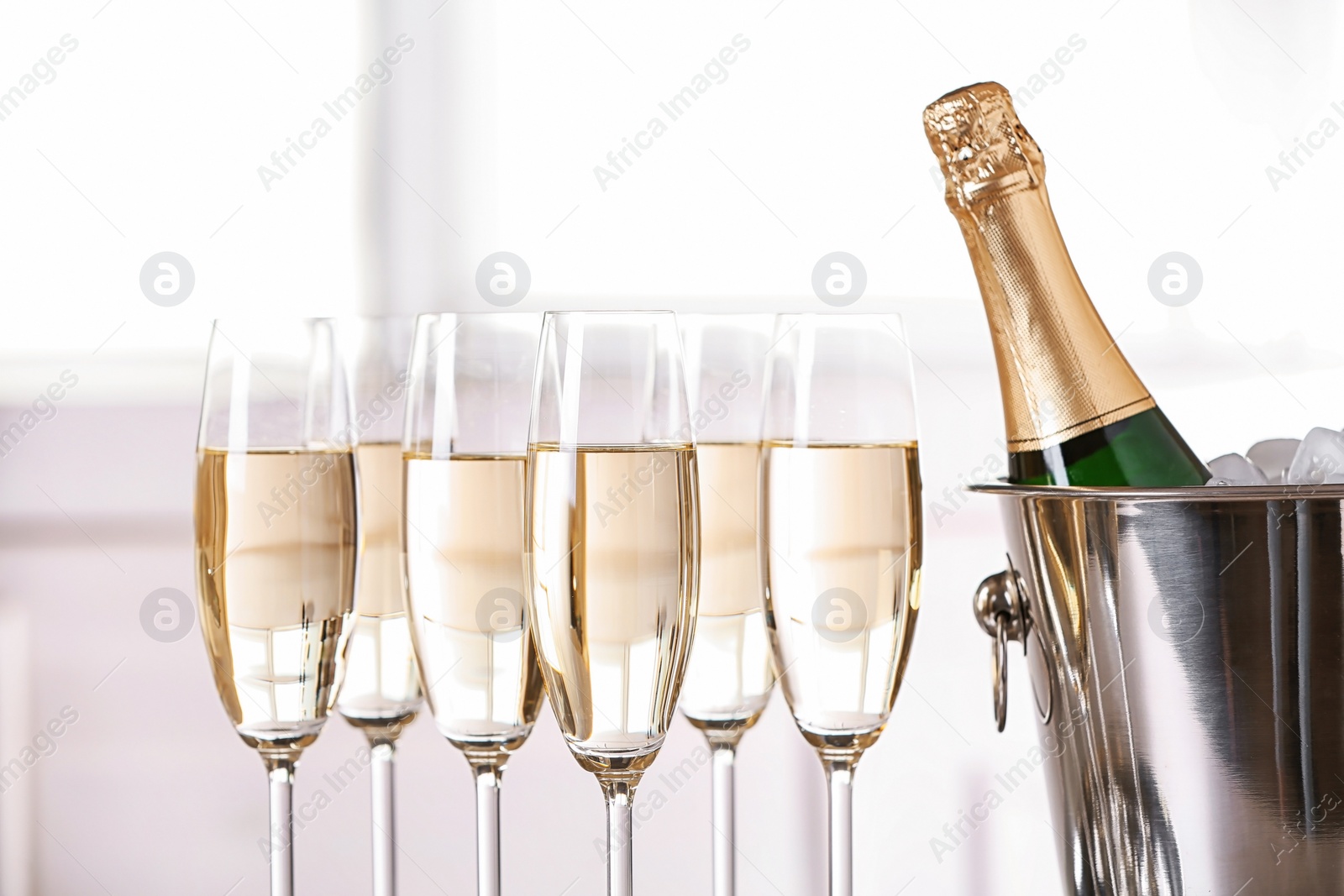 Photo of Glasses with champagne and bottle in bucket against blurred background