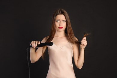 Photo of Upset young woman with flattening iron on black background. Hair damage