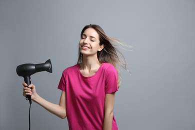 Photo of Beautiful young woman using hair dryer on grey background