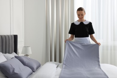 Photo of Young maid making bed in hotel room. Space for text