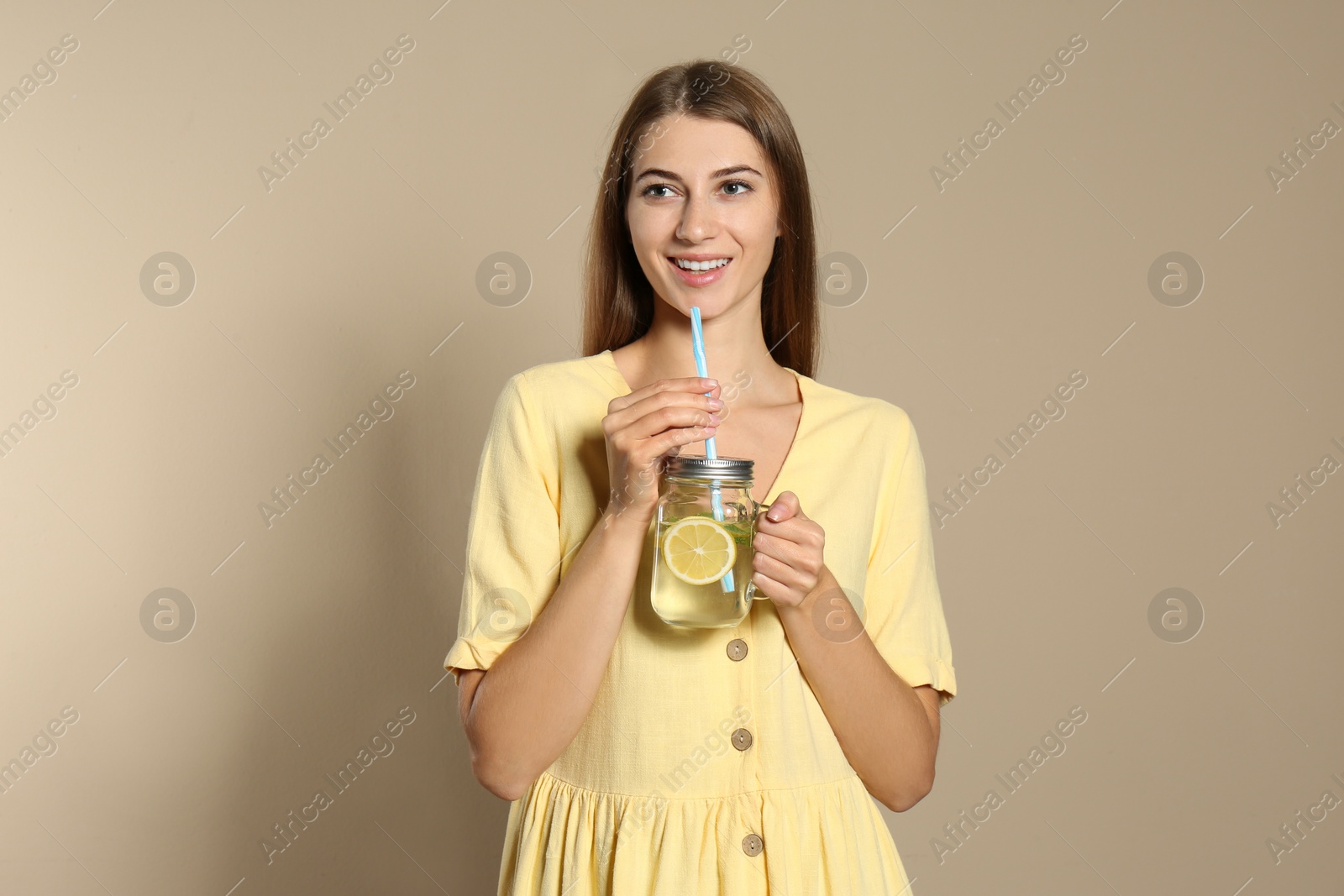 Photo of Young woman with glass of lemon water on beige  background