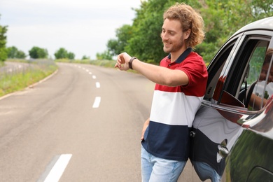 Attractive young man checking time near luxury car outdoors