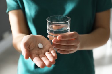 Photo of Young woman with abortion pill and glass of water on blurred background, closeup