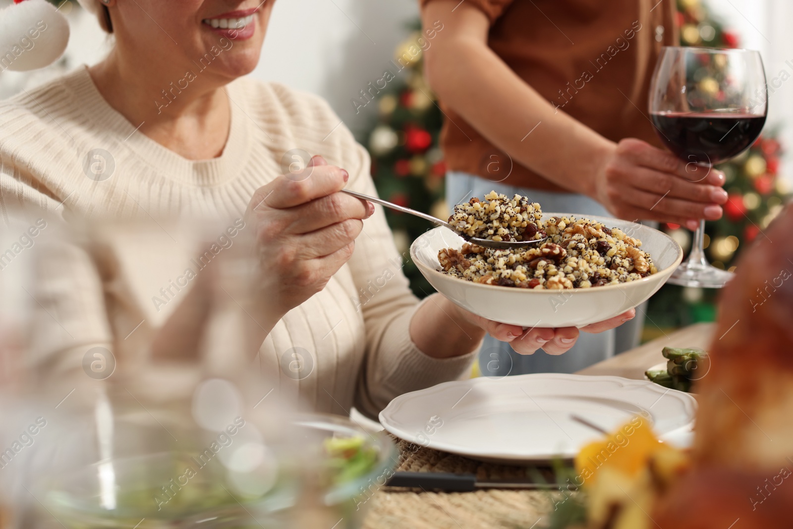 Photo of Woman with bowl of traditional Christmas kutia and her family at festive dinner, closeup. Slavic dish