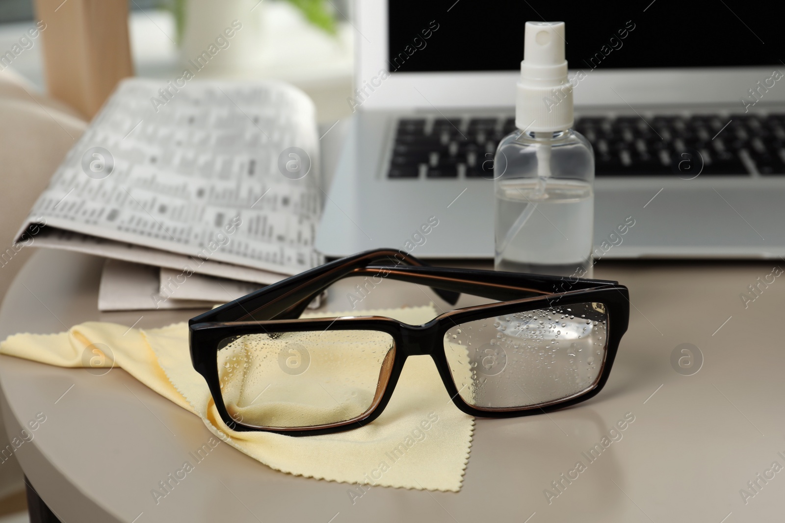 Photo of Glasses, microfiber cloth and spray bottle on table indoors