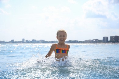 Photo of Emotional little girl having fun in sea on sunny day. Beach holiday