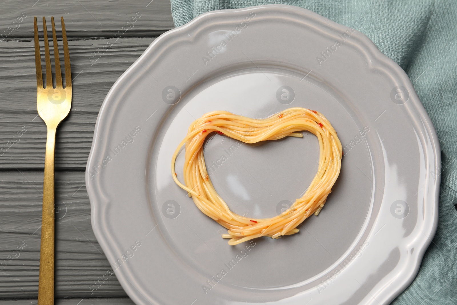 Photo of Heart made with spaghetti and fork on grey wooden table, top view