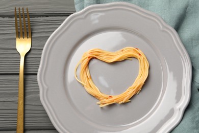 Photo of Heart made with spaghetti and fork on grey wooden table, top view