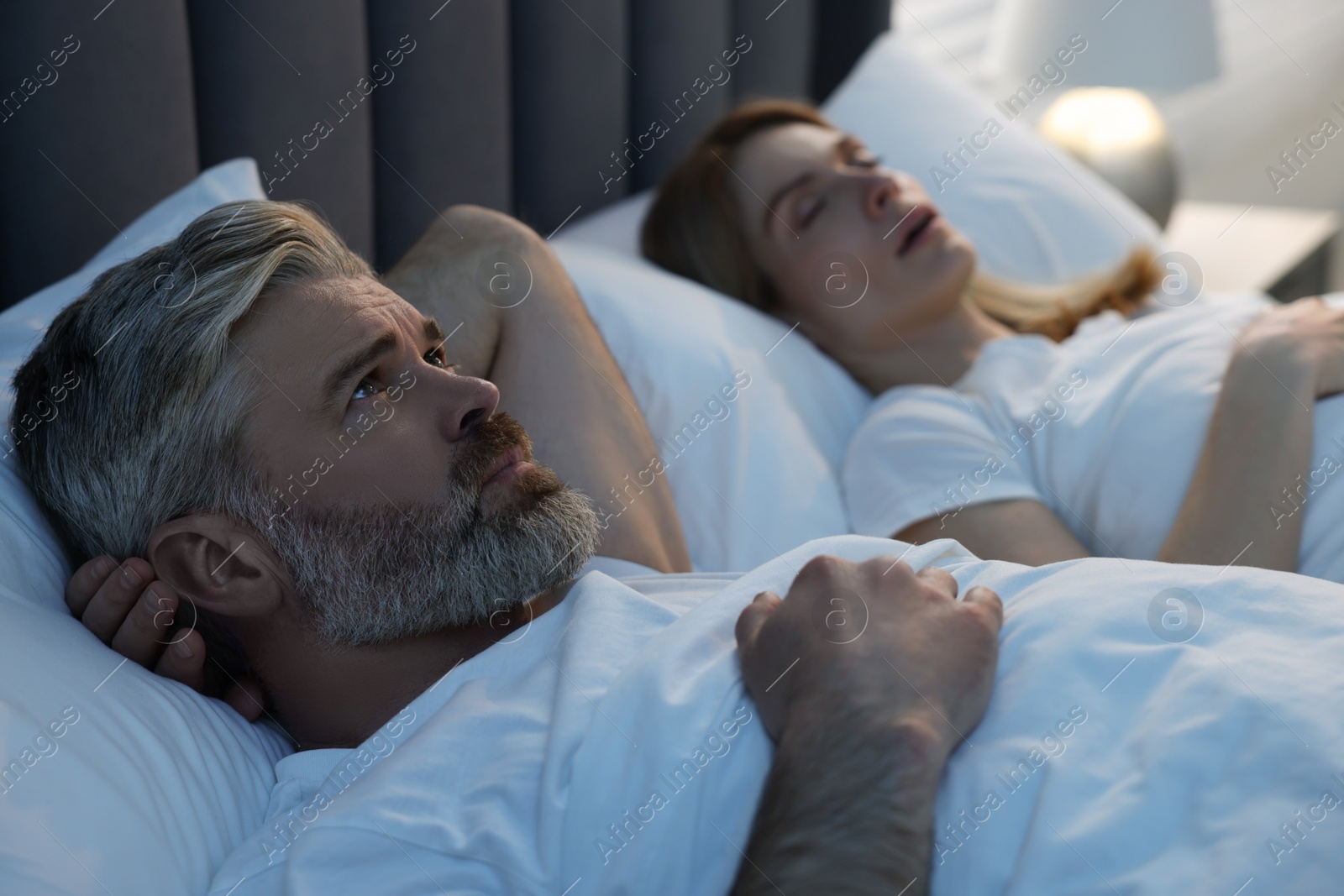 Photo of Irritated man lying near his snoring wife in bed at home