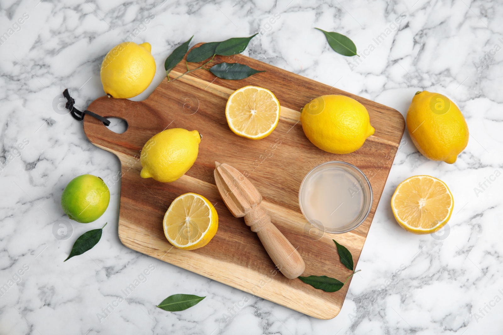 Photo of Wooden citrus reamer, juice, fresh lemons and lime on white marble table, flat lay