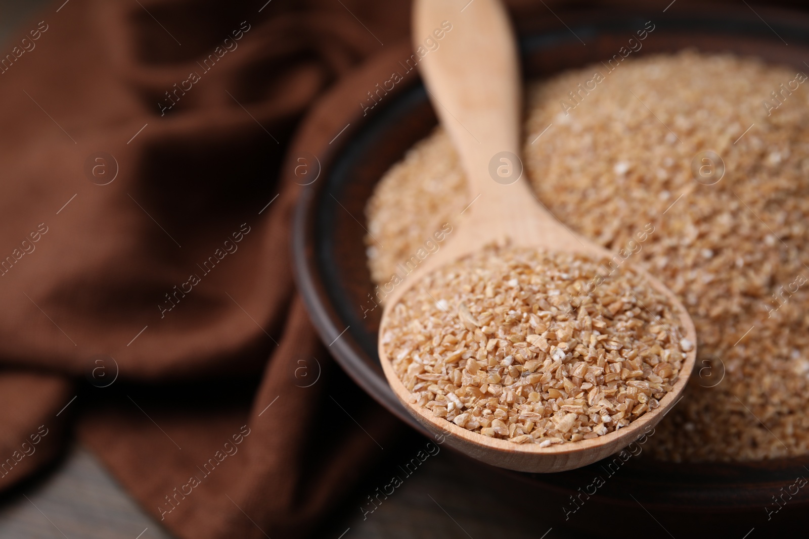 Photo of Dry wheat groats in bowl and spoon on table, closeup. Space for text