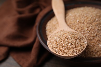 Photo of Dry wheat groats in bowl and spoon on table, closeup. Space for text