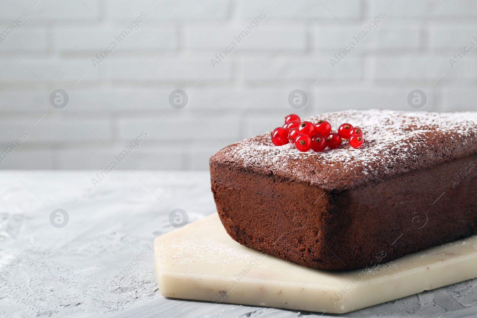 Photo of Tasty chocolate sponge cake with powdered sugar and currant on light grey textured table, closeup. Space for text