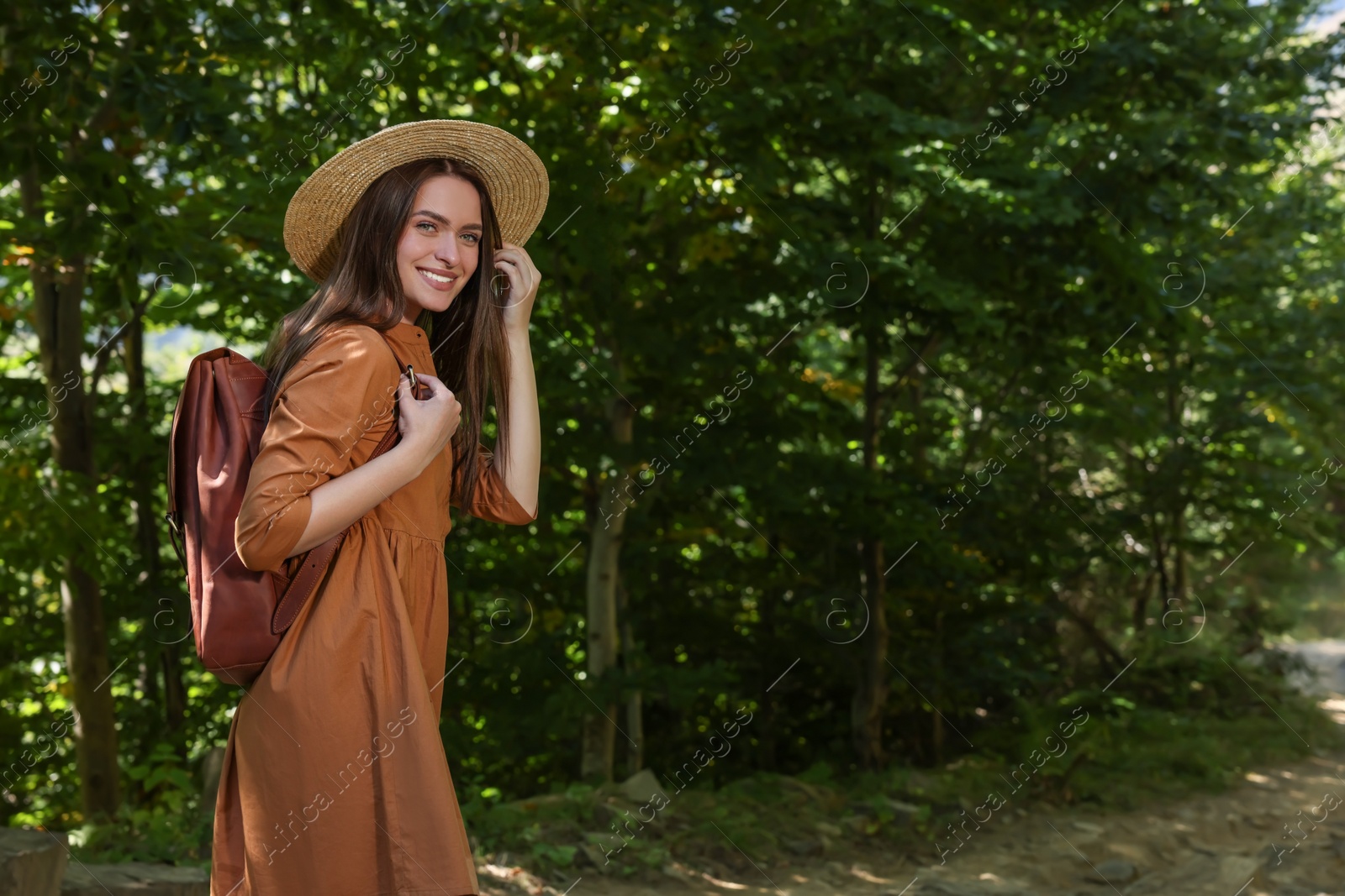 Photo of Happy woman with backpack and hat enjoying her walk in forest