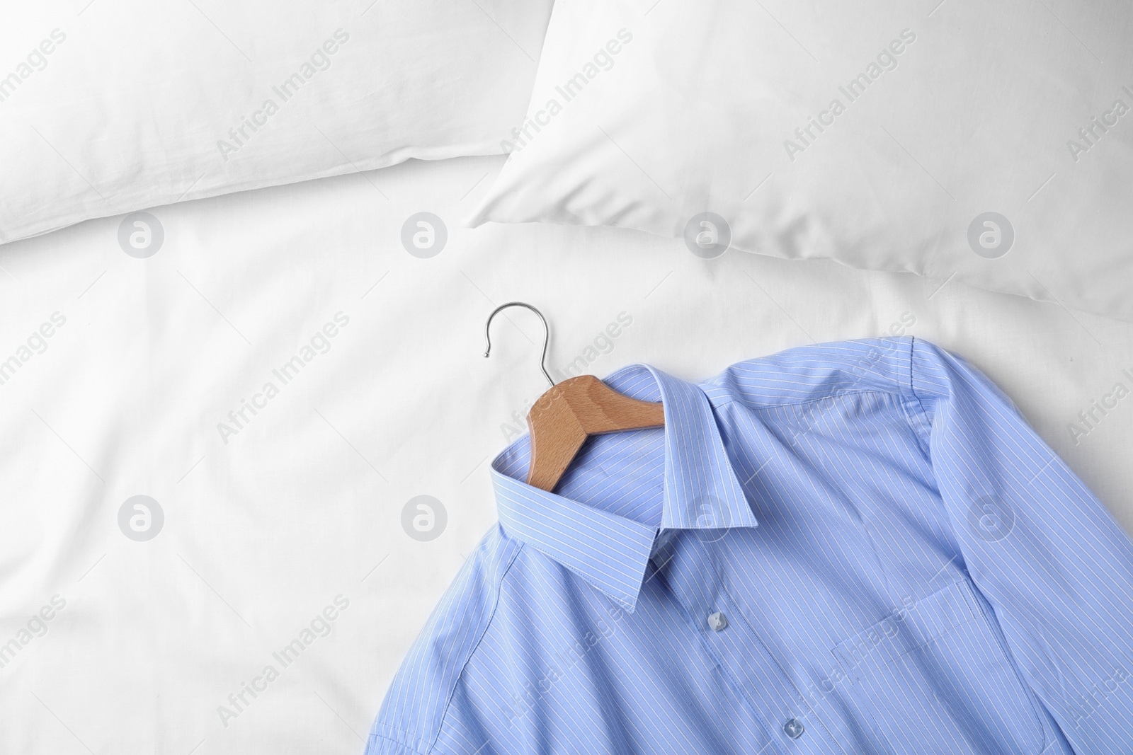 Photo of Stylish light blue shirt on bed, space for text. Dry-cleaning service