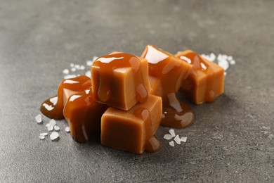 Yummy caramel candies with sauce and sea salt on grey table, closeup