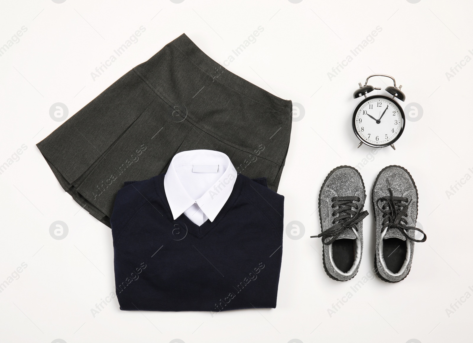 Photo of School uniform for girl and alarm clock on white background, top view