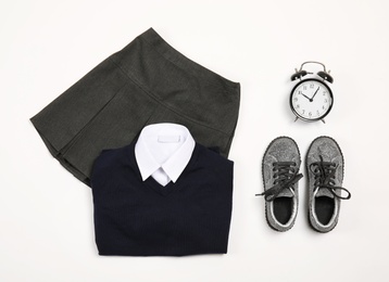 School uniform for girl and alarm clock on white background, top view