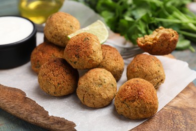 Delicious falafel balls with sauce on wooden board, closeup