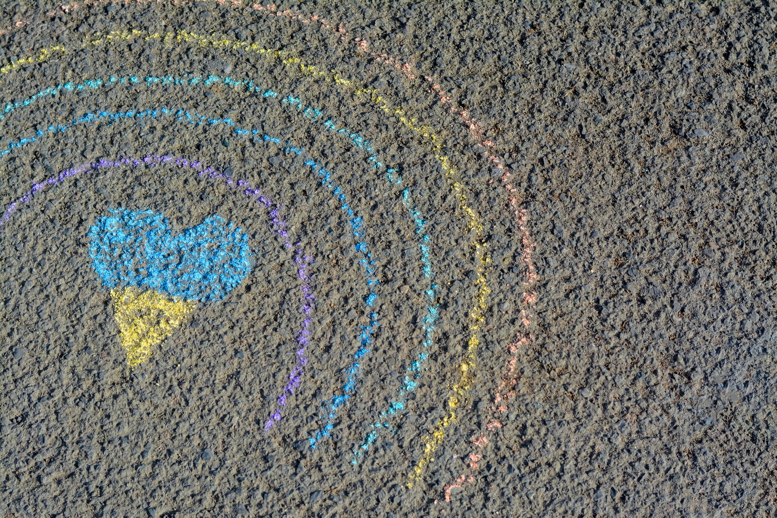 Photo of Rainbow with heart drawn by blue and yellow chalk on asphalt, top view