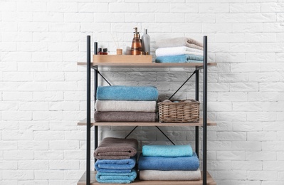 Photo of Shelving unit with clean towels and toiletries near brick wall