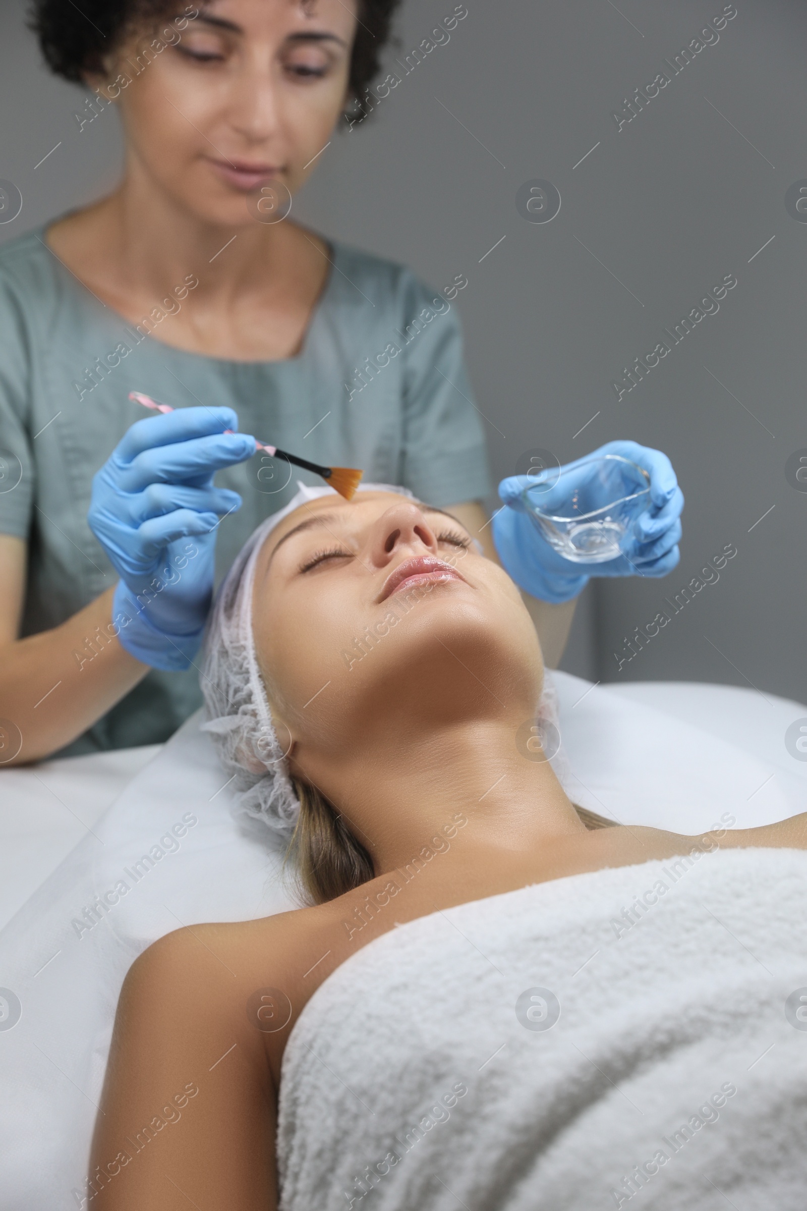 Photo of Cosmetologist applying chemical peel product on client's face in salon