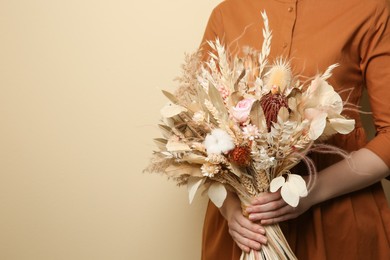 Photo of Woman holding beautiful dried flower bouquet on beige background, closeup. Space for text