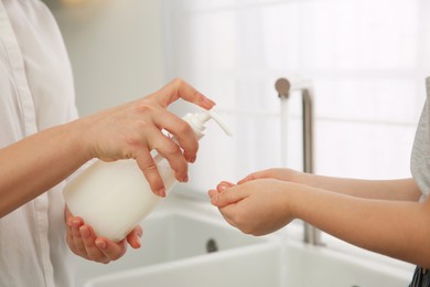 Photo of Mother and daughter washing hands with liquid soap together at home, closeup