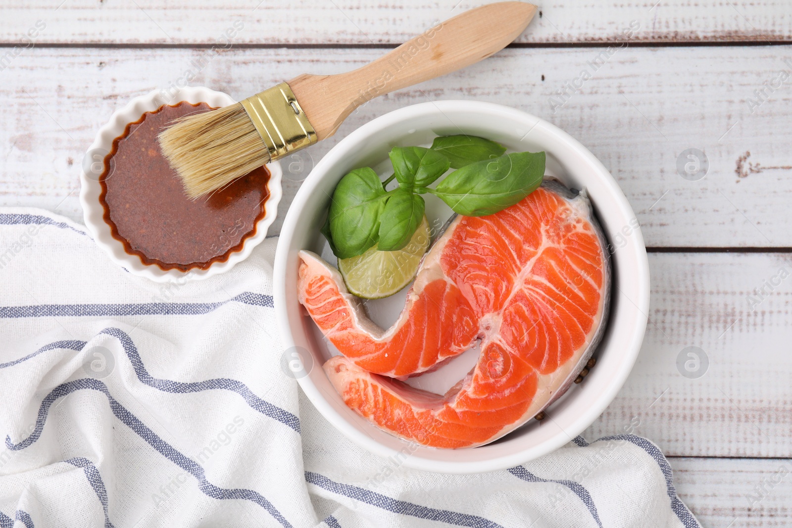 Photo of Fresh marinade, fish, brush and lime on white wooden table, top view