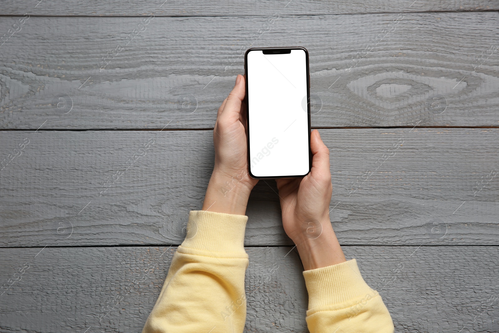 Photo of Woman with smartphone at grey wooden table, top view