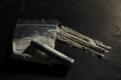 Drug addiction. Plastic bag with cocaine and rolled dollar banknote on grey textured table, closeup