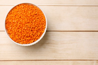 Photo of Raw lentils in bowl on wooden table, top view. Space for text