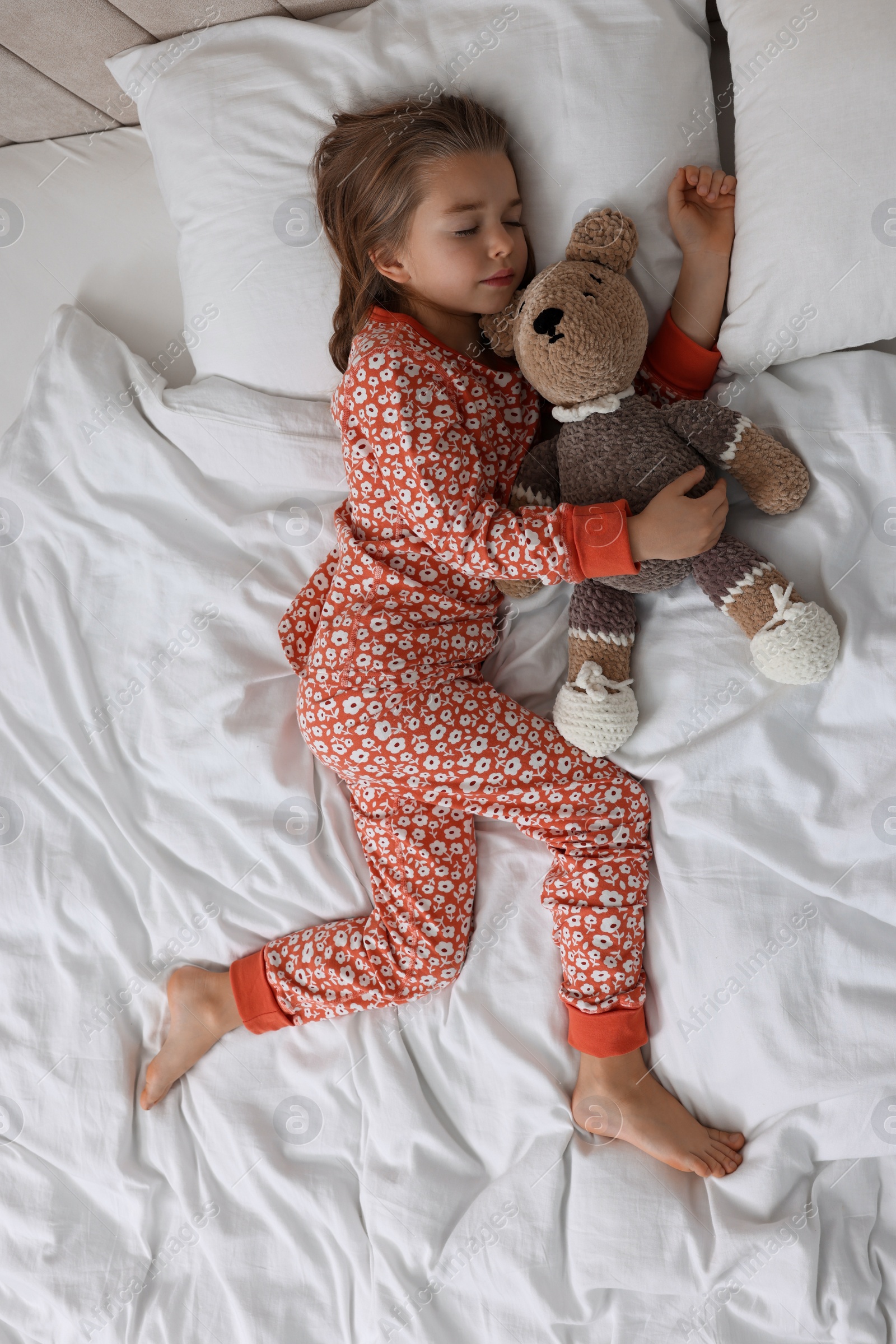 Photo of Cute little girl with toy bear sleeping on bed, top view