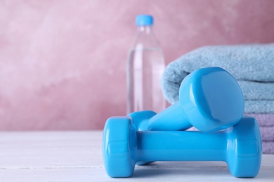 Stylish dumbbells, towels and bottle of water on table against color background, space for text. Home fitness