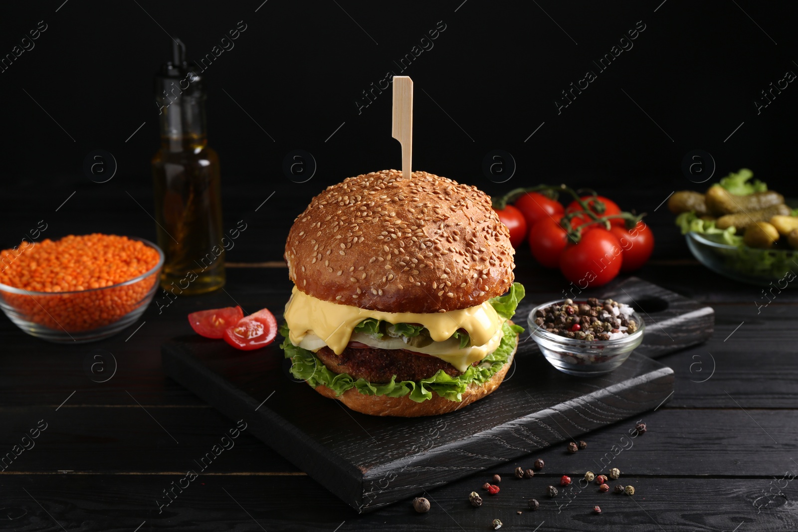 Photo of Tasty vegetarian burger and ingredients on black wooden table