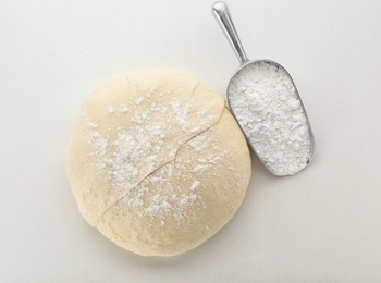 Photo of Raw wheat dough and scoop with flour on white background, top view