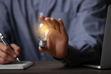 Photo of Glow up your ideas. Closeup view of man holding light bulb while working at wooden desk