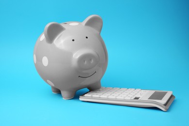 Piggy bank and calculator on light blue background