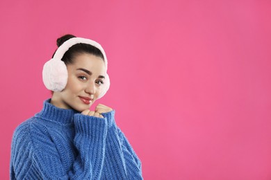 Photo of Beautiful young woman wearing earmuffs on pink background. Space for text