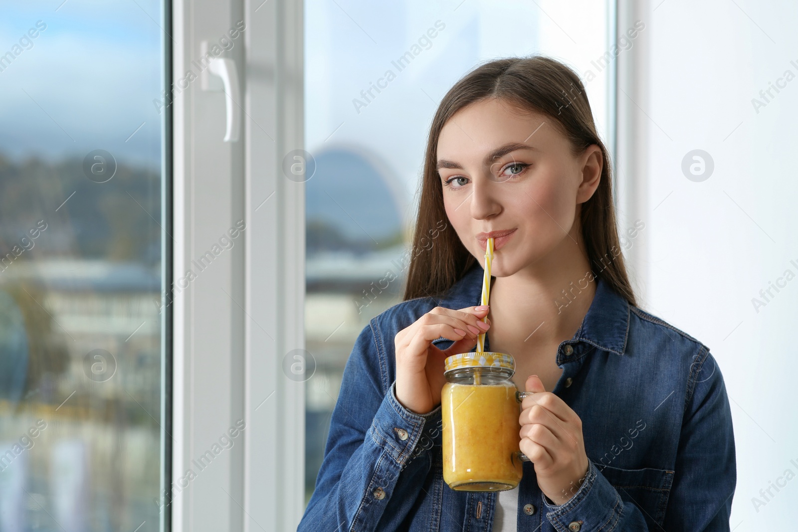 Photo of Beautiful young woman drinking delicious smoothie near window. Space for text