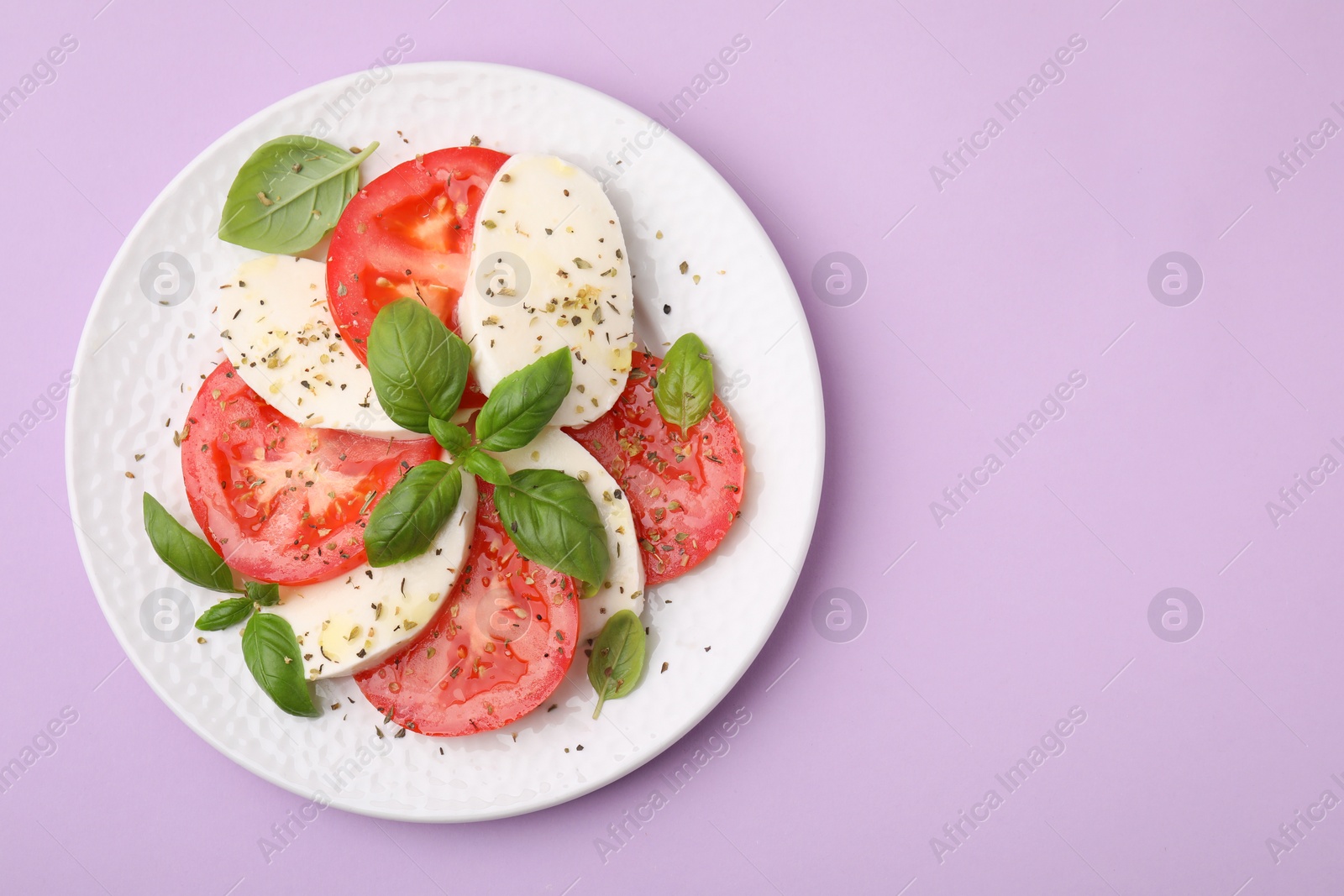 Photo of Plate of delicious Caprese salad with herbs on violet table, top view. Space for text