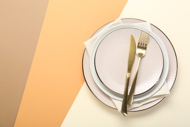 Photo of Ceramic plates, cutlery and napkin on color background, top view. Space for text