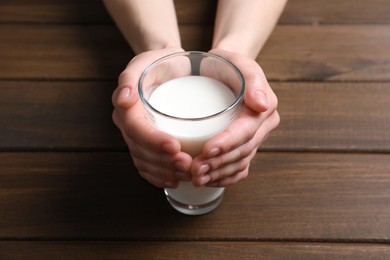 Photo of Woman holding glass of milk at wooden table, closeup