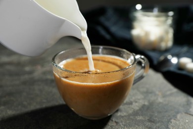 Photo of Pouring milk into cup of coffee on grey table, closeup