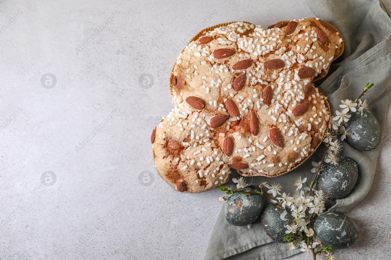 Photo of Delicious Italian Easter dove cake (Colomba di Pasqua), flowers and decorated eggs on grey table, flat lay. Space for text