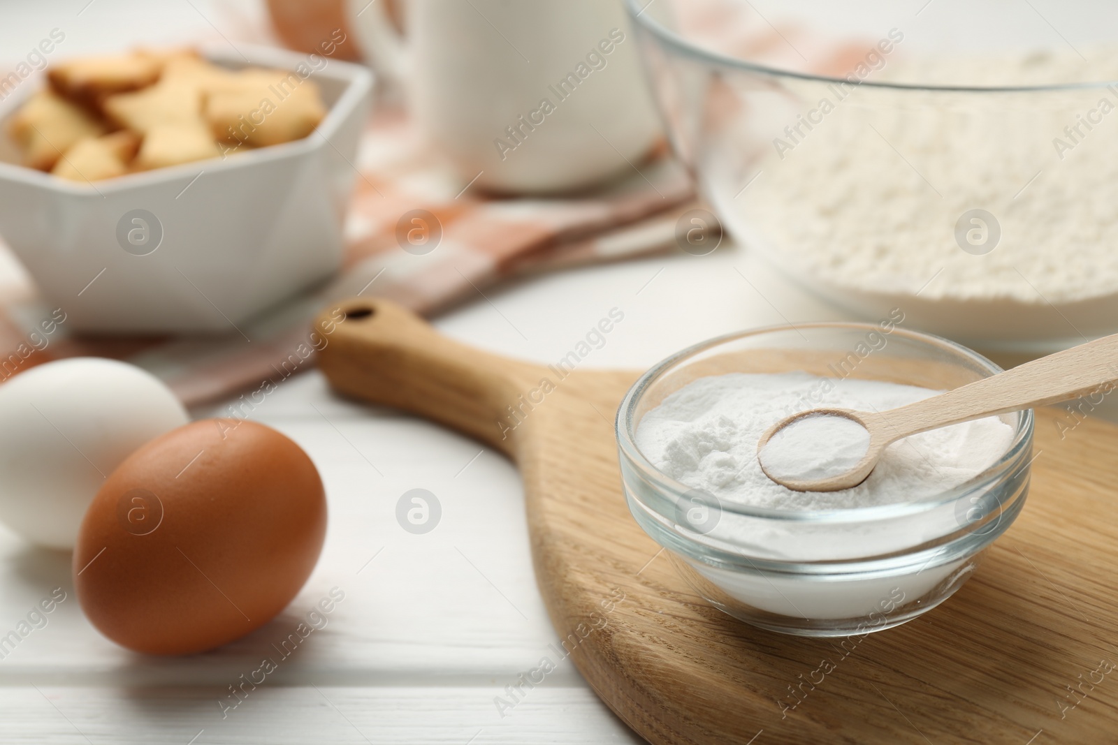 Photo of Baking powder in bowl and eggs on white wooden table, closeup