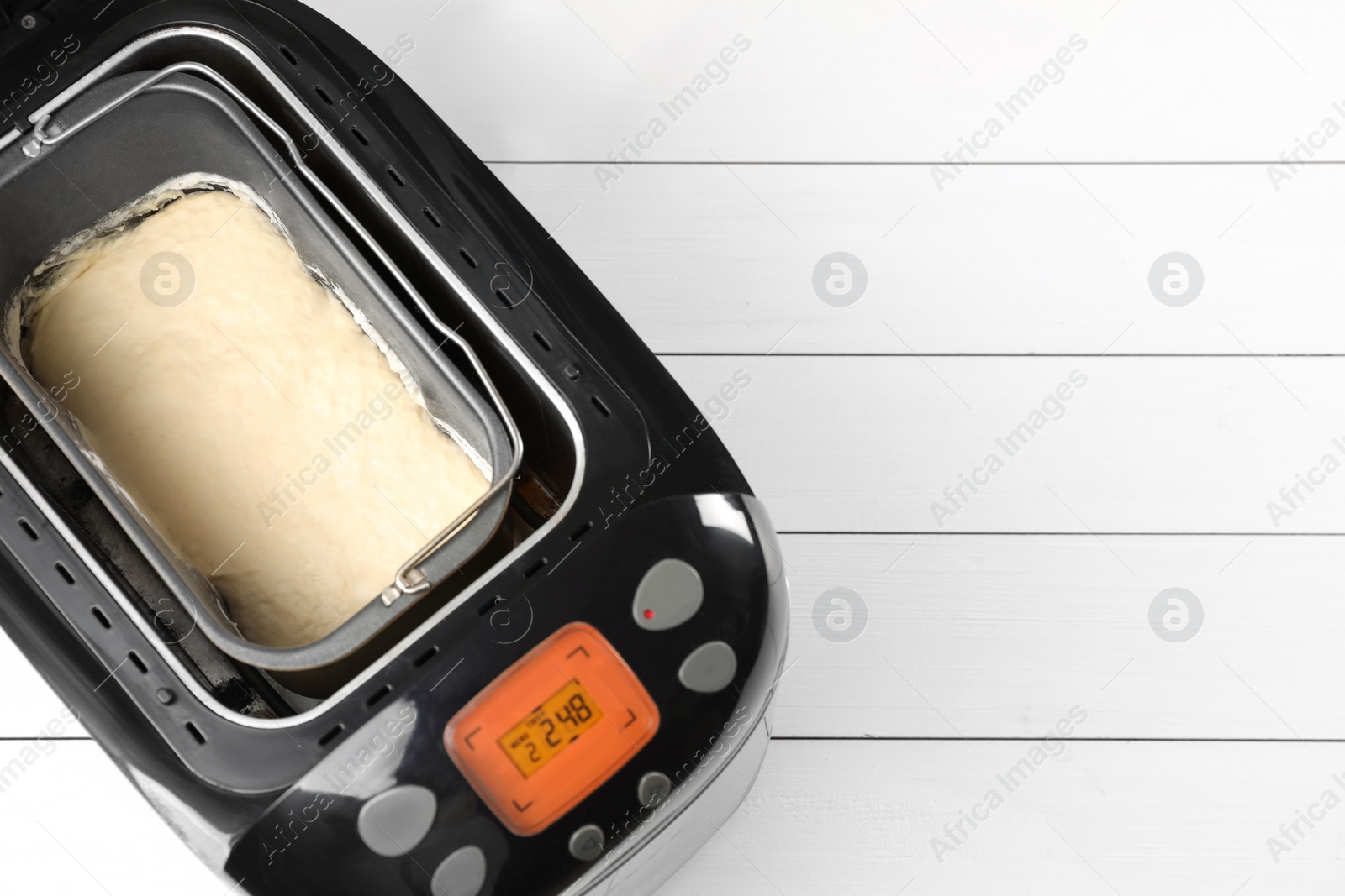 Photo of Breadmaker with raw dough on white wooden table, top view. Space for text