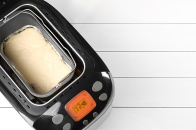 Photo of Breadmaker with raw dough on white wooden table, top view. Space for text